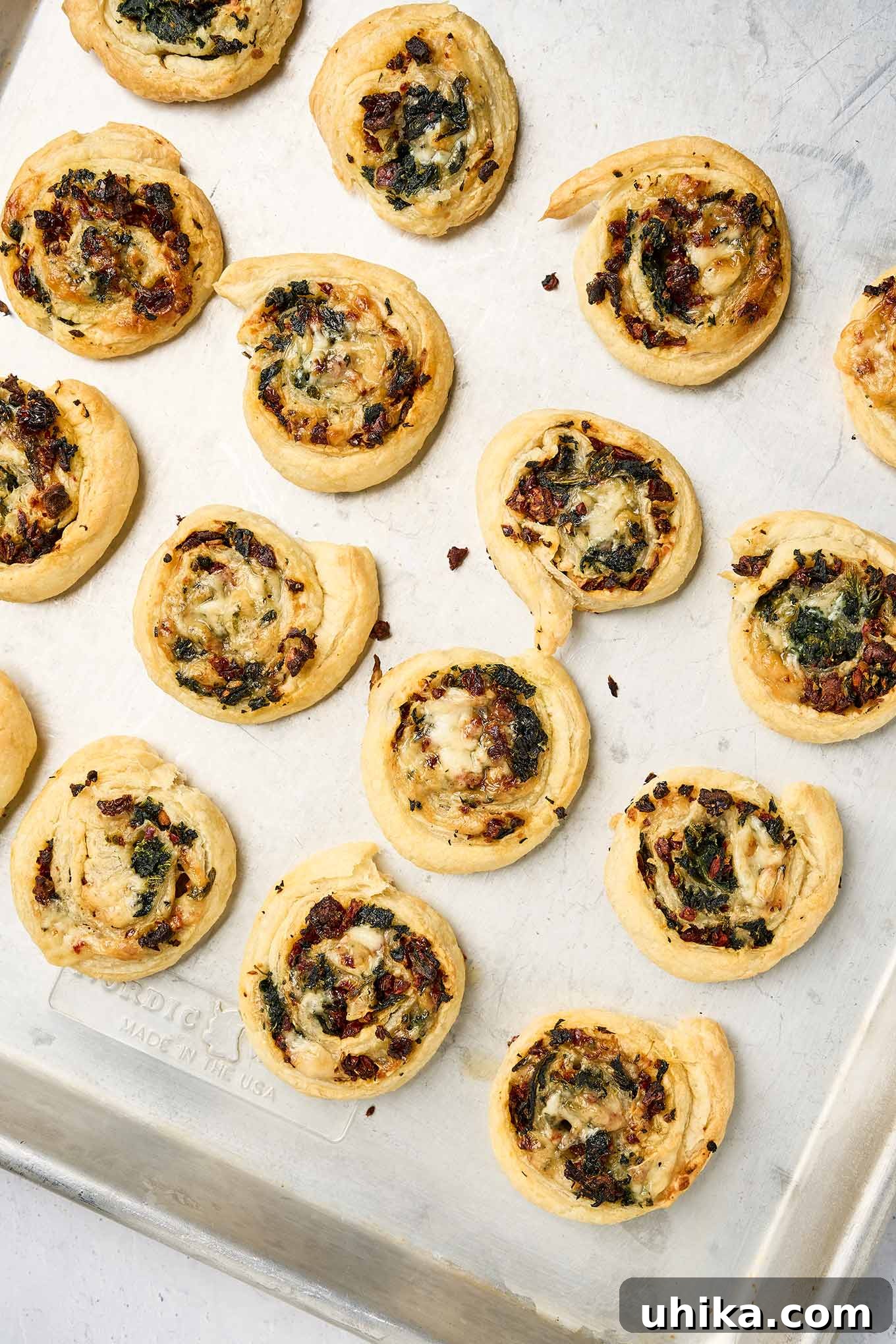 Savory Spinach Swirls 7 Golden spinach pinwheels, fresh from the oven, on a baking sheet, with crisp, puffed pastry and visible spinach and sun-dried tomatoes, illustrating the delicious finished product.