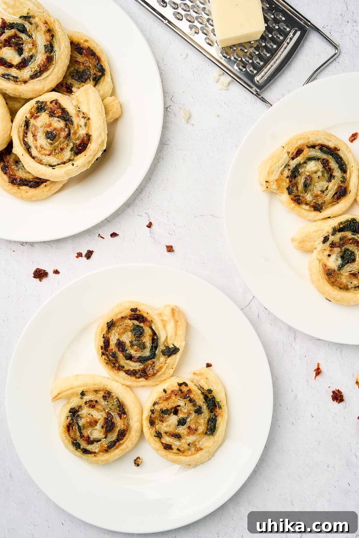 Savory Spinach Swirls 8 Plated spinach pinwheels made with puff pastry, spinach, sun-dried tomatoes, and cheese, shown from a top-down view on a white serving plate, garnished with fresh herbs.