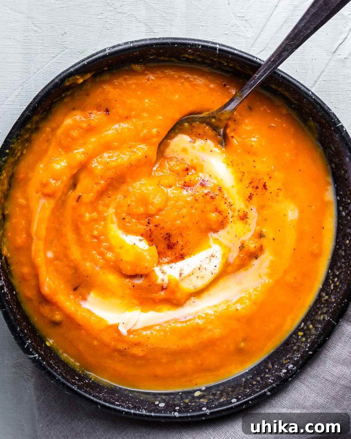 Silken Roasted Butternut Bliss 8 A close-up shot of rich butternut squash soup served in a dark bowl, elegantly topped with a swirl of cream and a dusting of nutmeg.