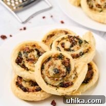 Golden spinach pinwheels made with puff pastry, spinach, sun-dried tomatoes, and cheese, stacked on a white plate, ready to be served as an appetizer.