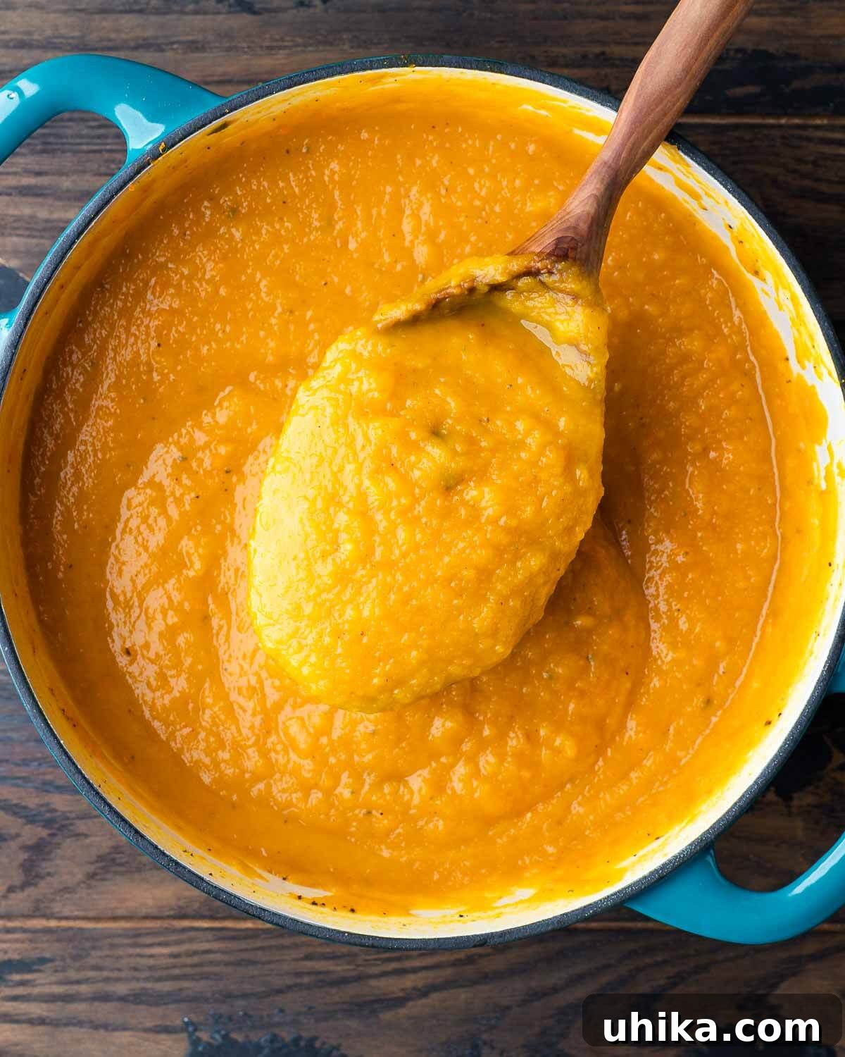 Silken Roasted Butternut Bliss 9 A large serving spoon elegantly scoops out a generous portion of creamy butternut squash soup from a rustic Dutch oven.