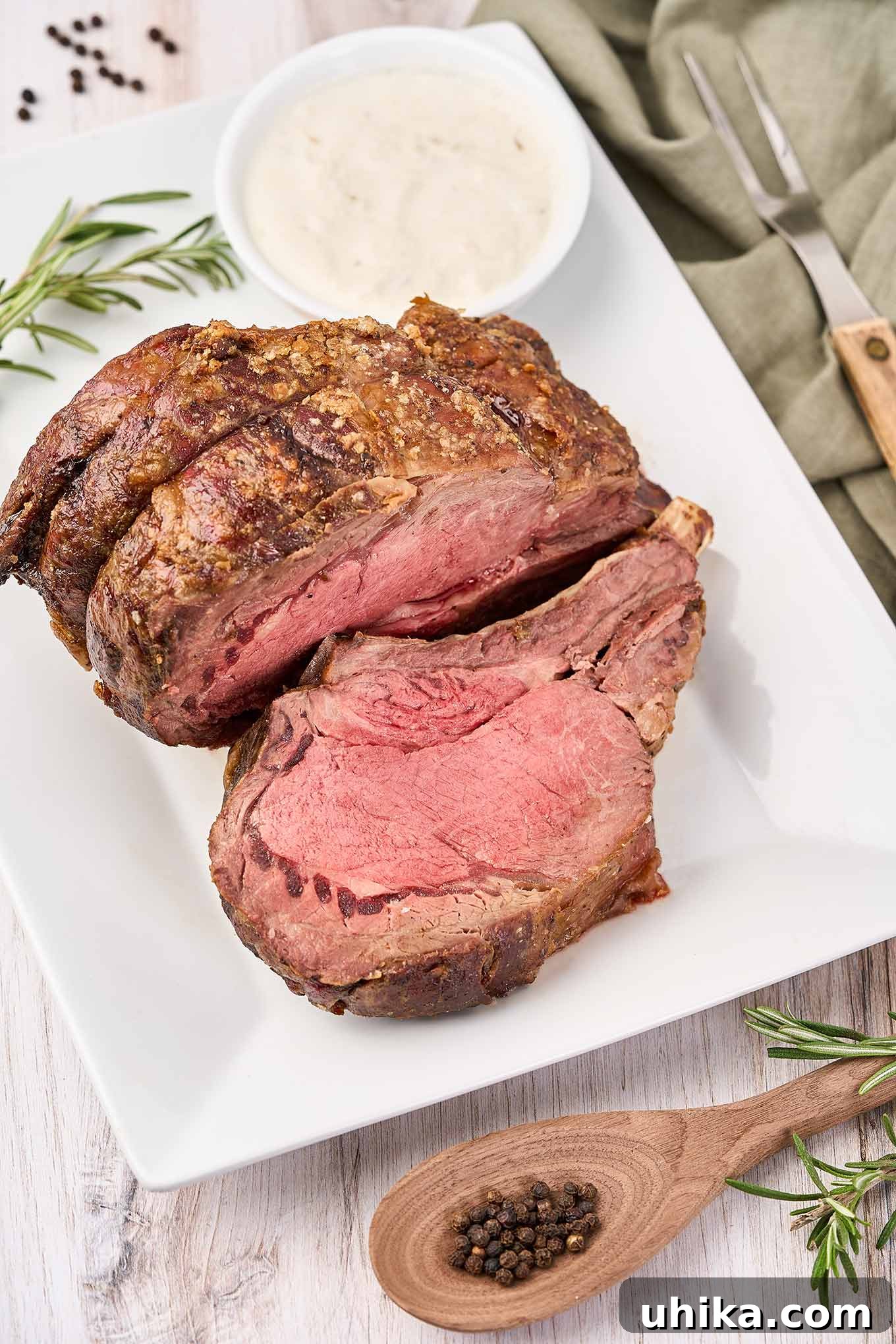 Mastering the Perfect Prime Rib 2 A perfectly roasted prime rib on a white serving platter, with one slice carved and a side of creamy horseradish sauce. Ideal for holiday feasts.