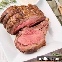 A white serving platter with a prime rib roast, one slice carved, horseradish sauce on the side.