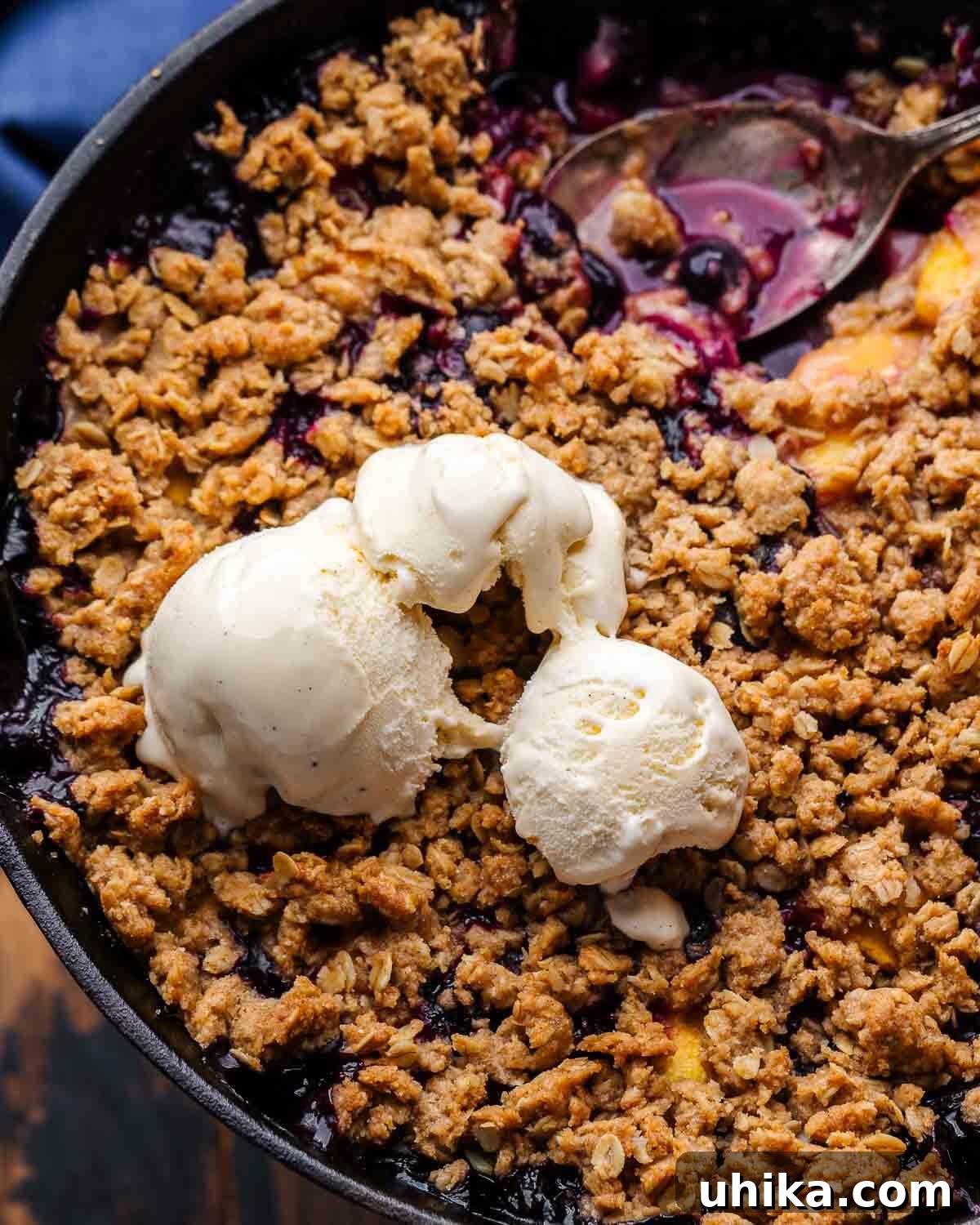 Sun-Kissed Peach and Blueberry Crumble 2 Closeup shot of peach blueberry crisp with melted vanilla ice cream, highlighting the golden oat topping and juicy fruit.