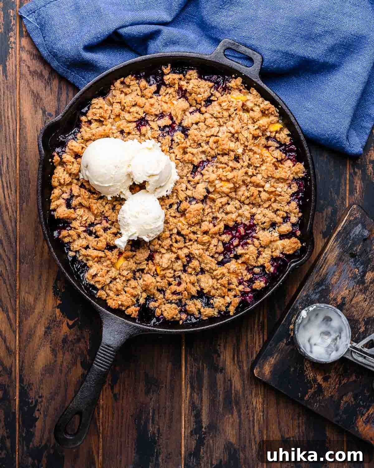 Sun-Kissed Peach and Blueberry Crumble 6 Overhead shot of peach blueberry crisp in cast iron pan with vanilla ice cream on top, ready to be served.