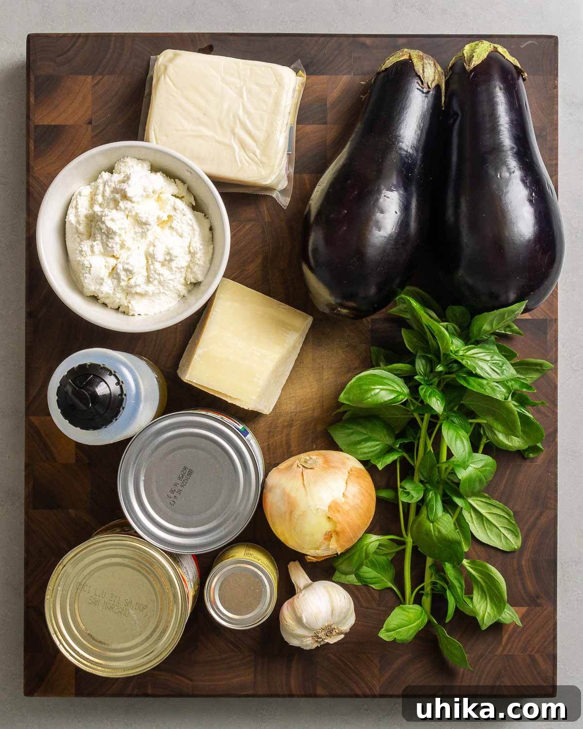 Roasted Eggplant Pasta Bake 3 Ingredients for baked eggplant pasta shown on a counter: mozzarella, ricotta, eggplant, Pecorino, olive oil, canned tomatoes, tomato paste, onion, garlic, and fresh basil.