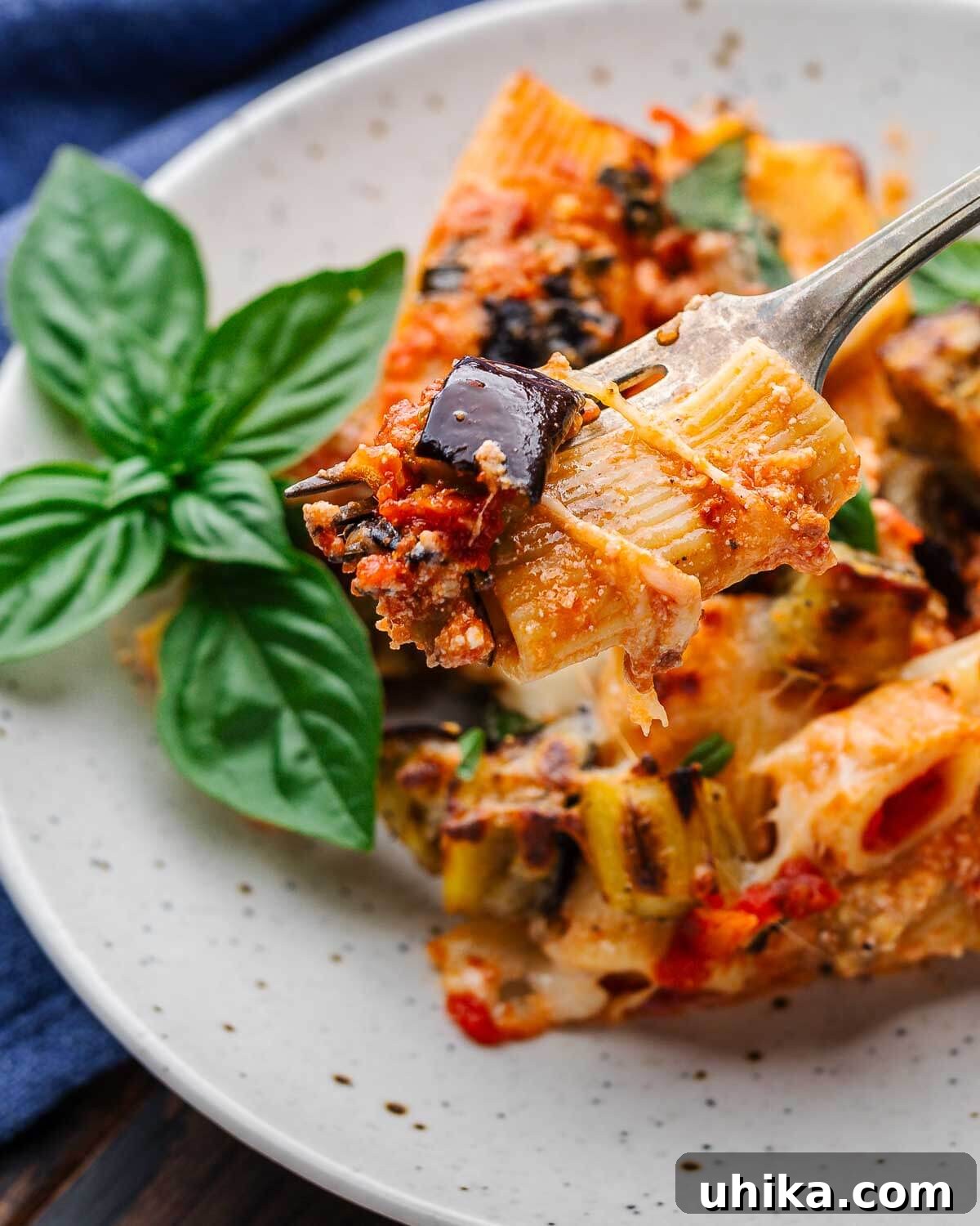 Roasted Eggplant Pasta Bake 10 Fork holding a piece of baked rigatoni with eggplant and melted cheese over a white plate.