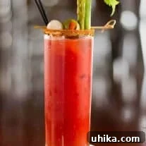 Zesty Red Reviver 3 Tall glass of Bloody Mary cocktail garnished with celery stalk, pickled asparagus, green olive, and cocktail onion, served with a spiced rim and black straw.