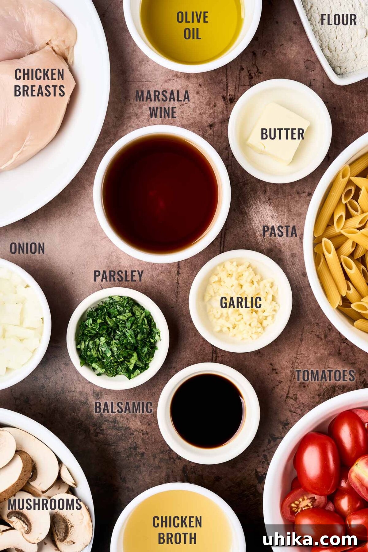Creamy Marsala Chicken Pasta with Burst Tomatoes 3 A labeled, overhead view of the ingredients for chicken Marsala pasta; chicken breasts, Marsala wine, penne pasta, mushrooms, garlic, onion, grape tomatoes, and more.