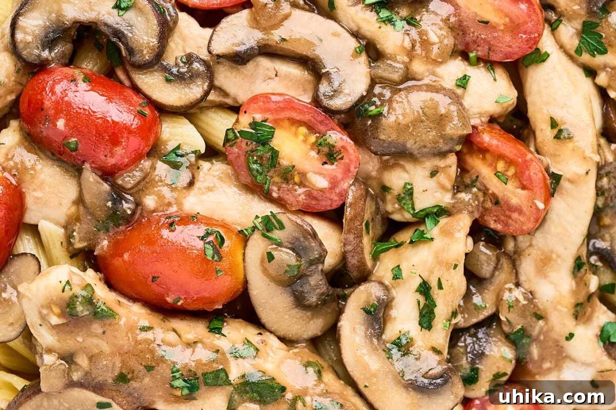 Creamy Marsala Chicken Pasta with Burst Tomatoes 8 A close up look at chicken Marsala pasta showing chicken breast strips, penne pasta, mushrooms, grape tomatoes, bits of garlic, and chopped parsley.