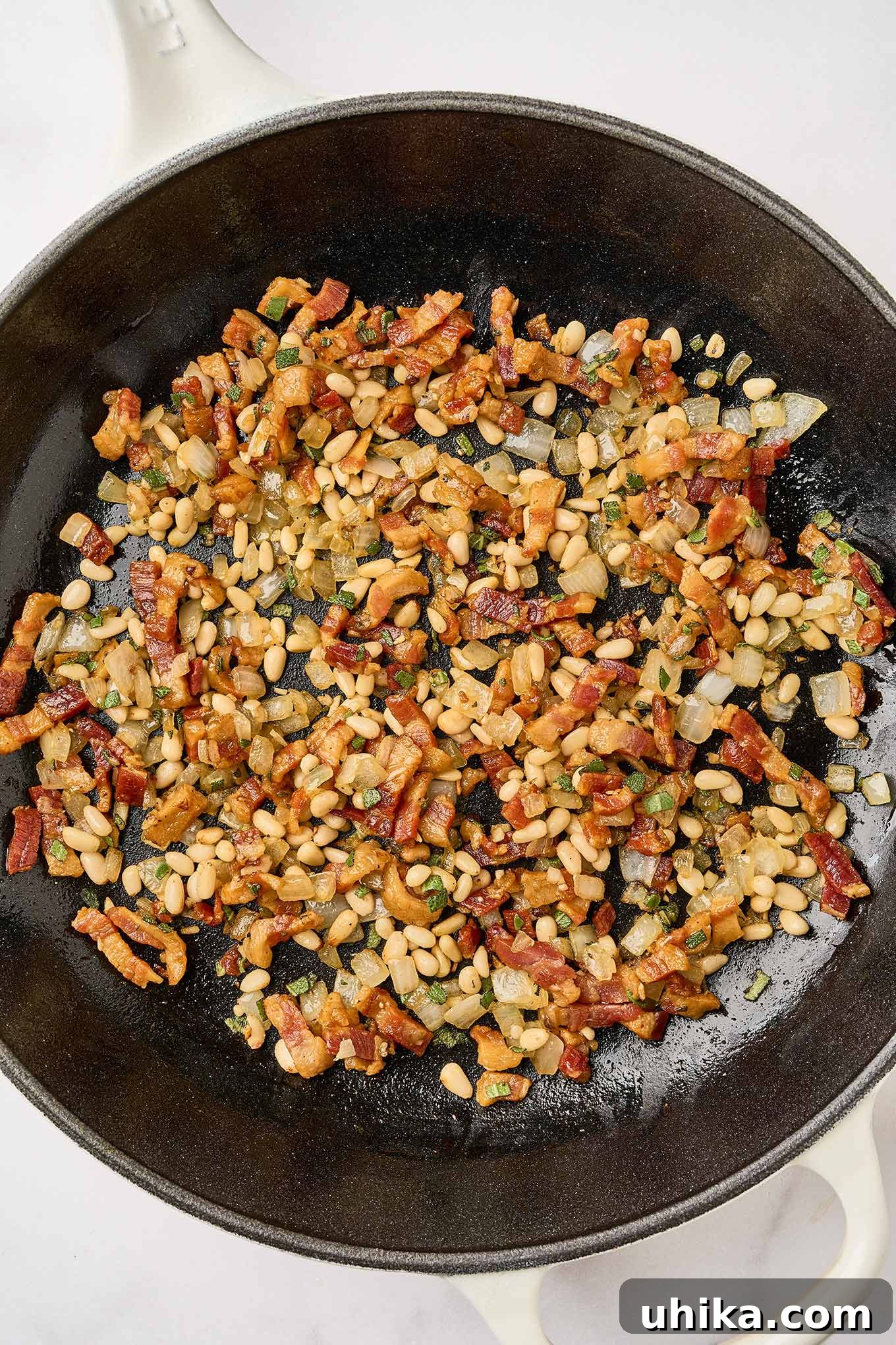 Golden Pumpkin Pasta with Crispy Pancetta and Creamy Parmesan 5 Preparing creamy pumpkin pasta, by combining fried pancetta with sautéed onions, garlic, and pine nuts in a cast iron skillet.