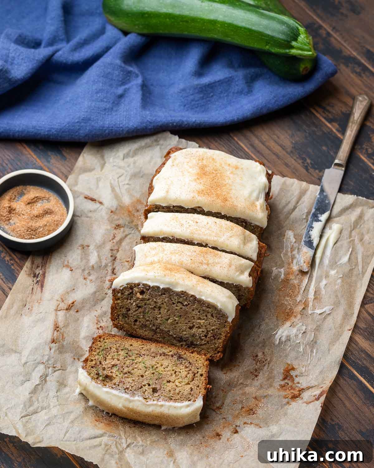 Moist Zucchini Loaf 7 Overhead shot of a perfectly cut zucchini bread with a generous layer of cream cheese frosting on top of parchment paper, ready to be enjoyed.