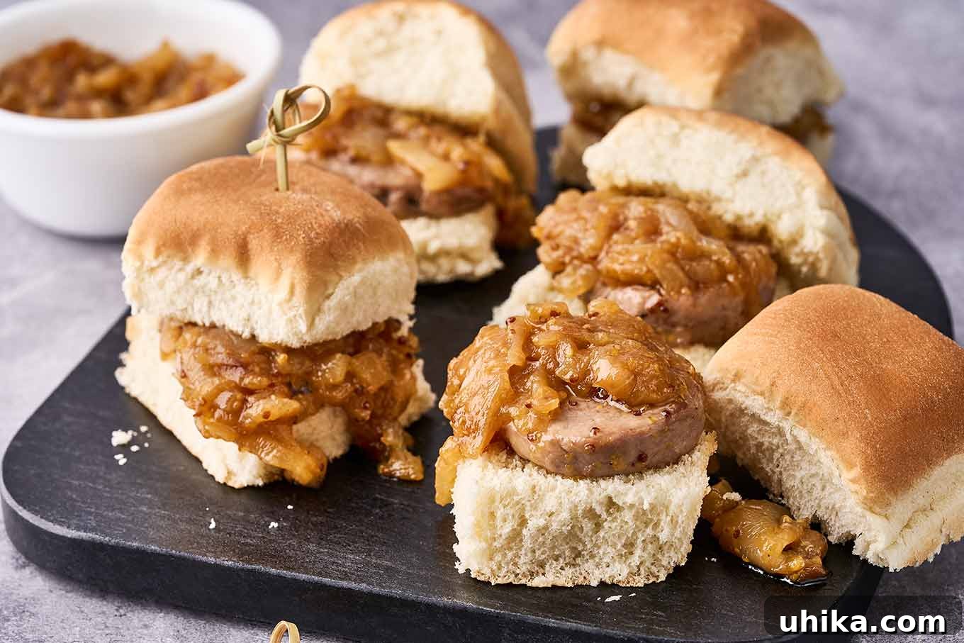 Maple Mustard Glazed Pork Tenderloin Sliders 5 A beautifully arranged black wooden cutting board showcasing five delightful pork sliders, one with the top bun removed to reveal the tender pork tenderloin slice and abundant caramelized onion topping, ready to be enjoyed as a perfect party snack or quick meal.