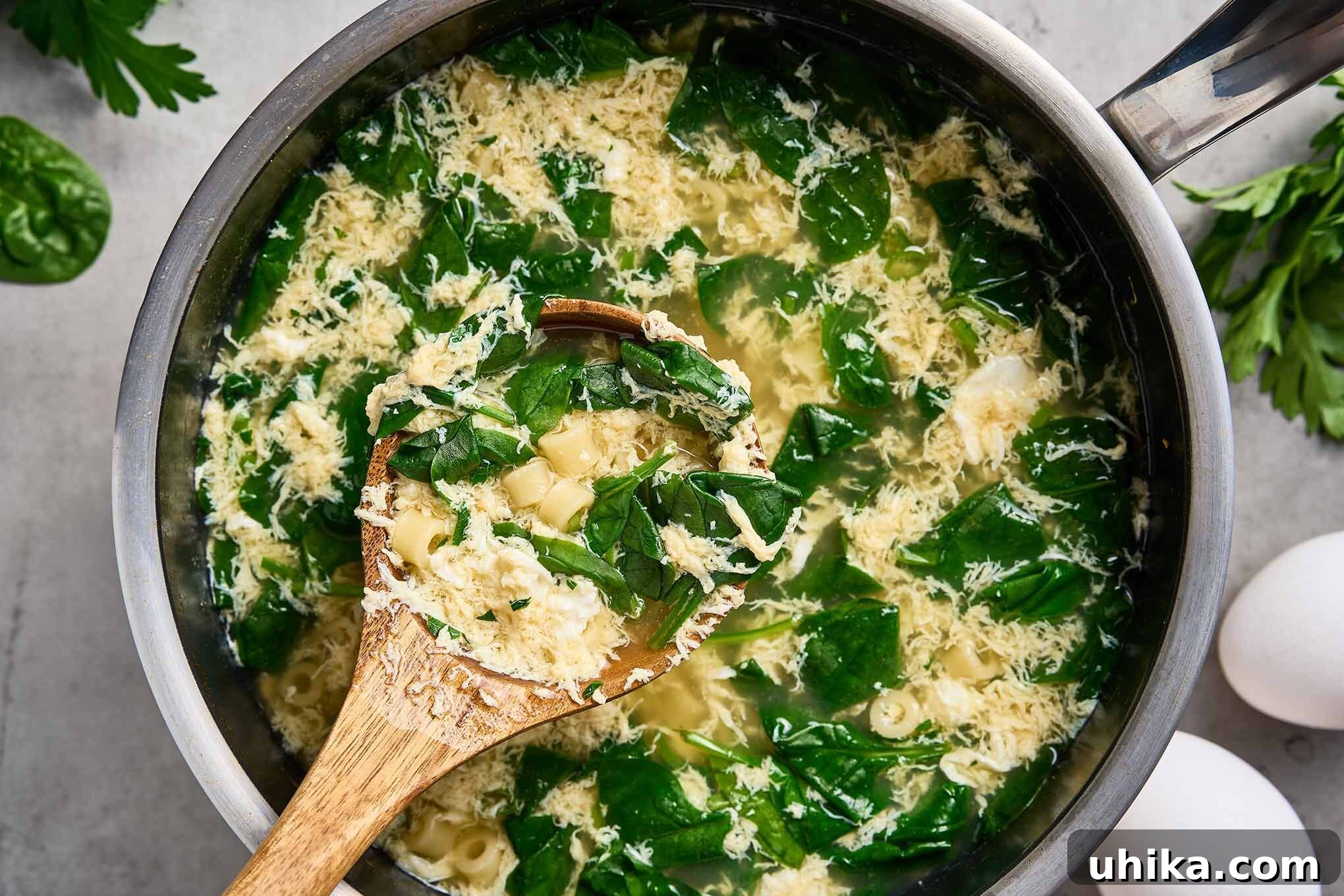 Silken Stracciatella with Fresh Spinach and Tender Pasta 6 Wooden spoon showing spinach, ditalini pasta, and egg ribbons lifted from a pot of stracciatella soup.