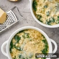 Bowls of stracciatella soup with spinach, ditalini, and grated Parmigiano-Reggiano, shown with bread and a cheese grater.