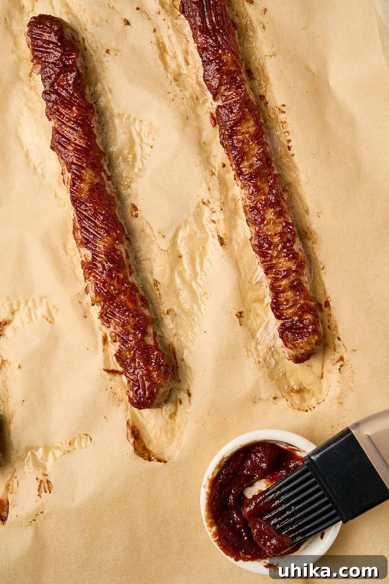 Golden Sausage Puffs 5 Three cooked Italian sausage logs, gently brushed with a rich tomato paste and balsamic vinegar mixture, laid atop strips of puff pastry, showcasing the preparation for savory sausage rolls.