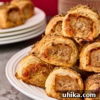 Puff pastry sausage rolls with golden, flaky layers and seasoned sausage filling shown stacked on a white serving plate.