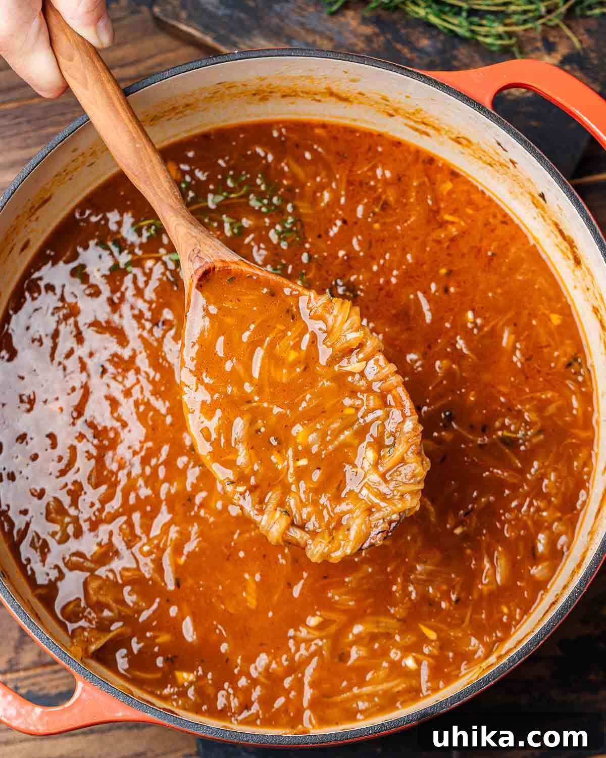 Caramelized Onion Elegance 8 Hands holding wooden ladle with French onion soup over a large Dutch oven, ready to serve.