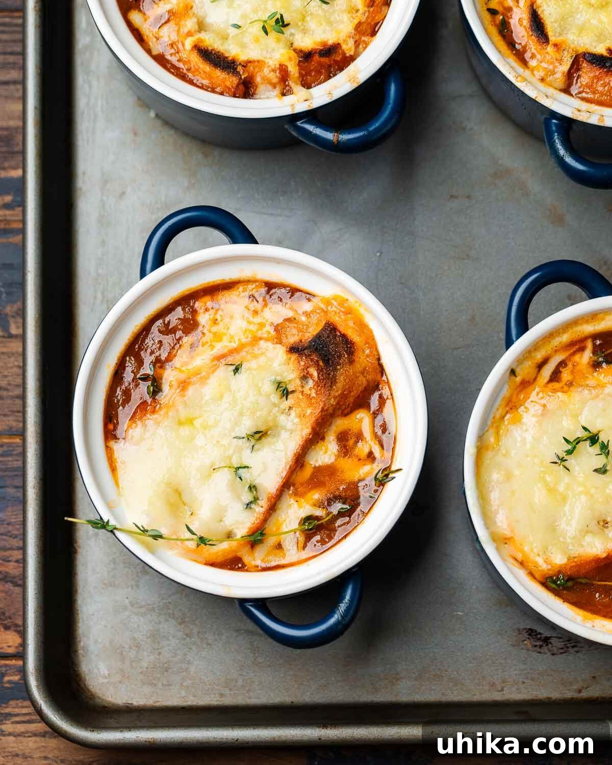 Caramelized Onion Elegance 9 Overhead shot of four blue crocks with baked French onion soup on a baking sheet, garnished with fresh thyme.
