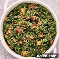 An overhead view of a casserole of sautéed sweet and sour spinach with bacon bits, sweet and sour sauce, and cream.