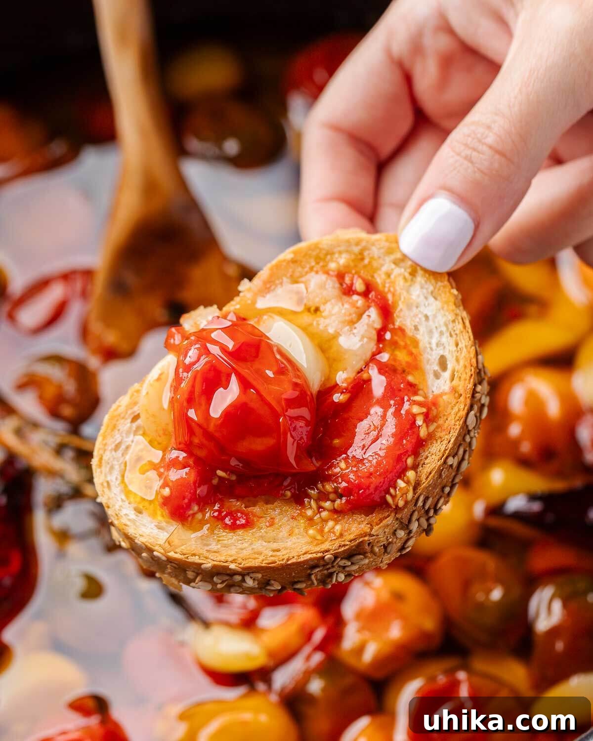 Rich Roasted Tomato Jewels 5 A hand holding a piece of crusty bread generously topped with homemade tomato confit.