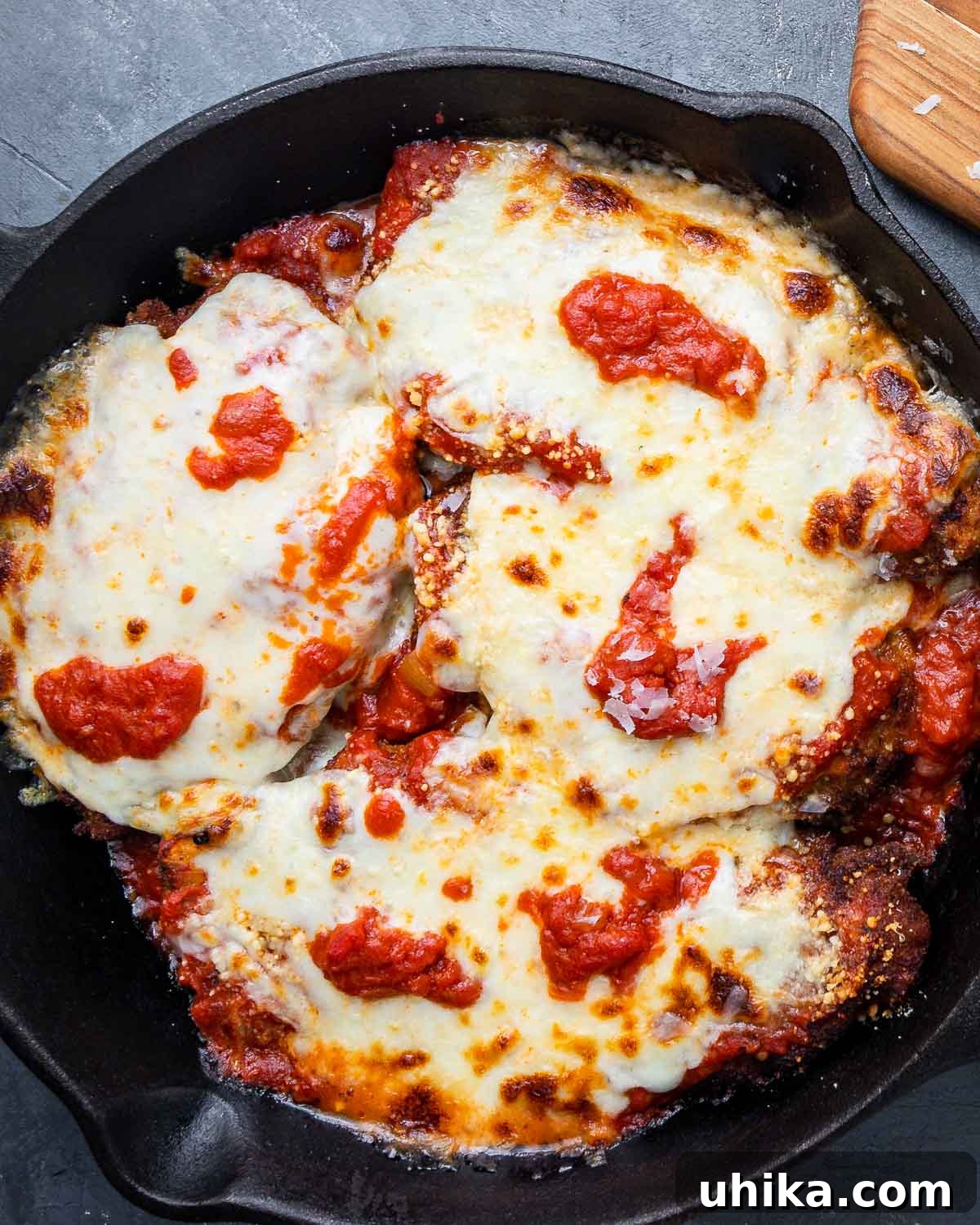 Overhead shot of cooked chicken parm in cast iron pan on blue board.