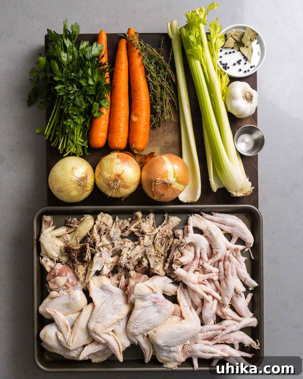 Homemade Liquid Gold 3 A vibrant display of fresh ingredients for chicken stock: parsley, carrots, thyme, celery, peppercorns, bay leaves, garlic, vinegar, onions, chicken wings, chicken feet, and chicken backbones laid out on a clean surface.