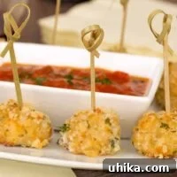 A close view of crispy chicken bites skewered with loop-ended bamboo skewers surrounding a small bowl of marinara dipping sauce.