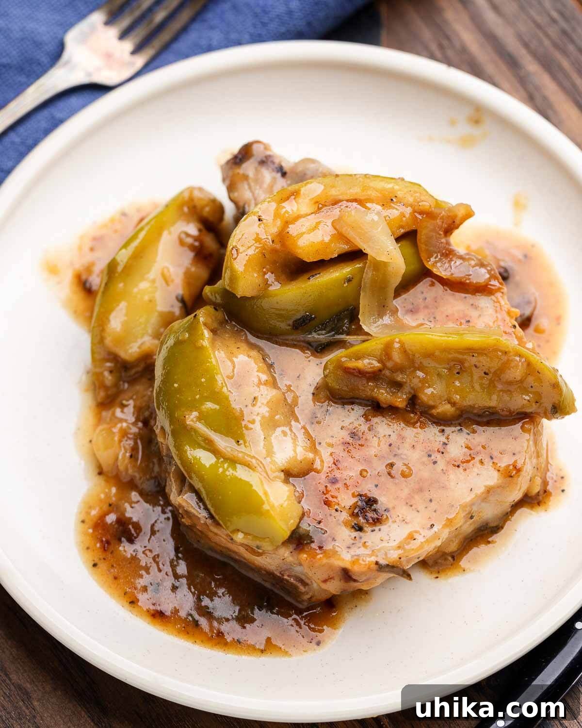 White plate with a perfectly seared pork chop, caramelized apples, and a rich, glossy sauce on a rustic wooden table, embodying the warmth of fall dinner.