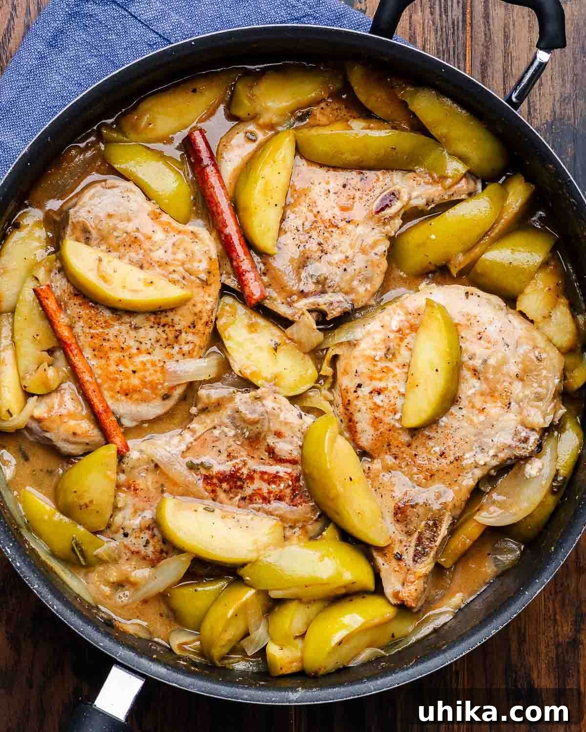 Overhead shot of a large black pan filled with beautifully cooked pork chops, tender apples, and onions swimming in a rich, glossy sauce, ready to serve.