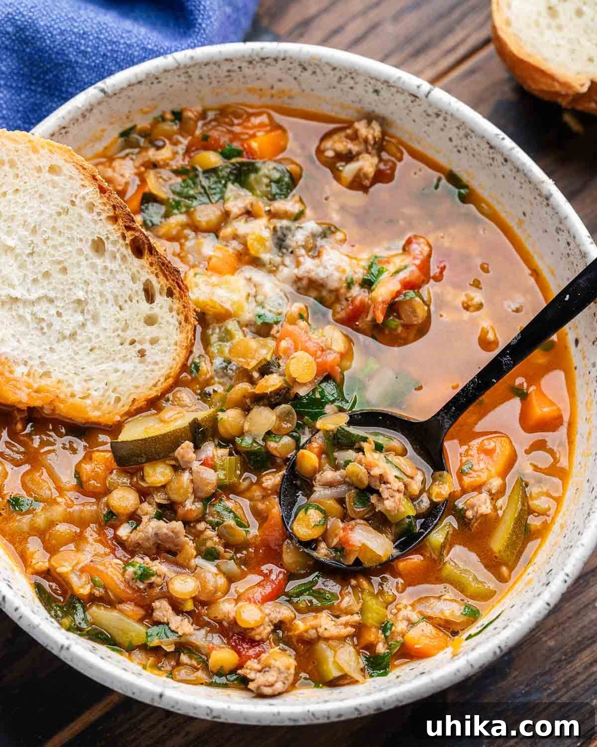 Rustic Sausage and Lentil Pot 2 Sausage lentil soup in white bowl with slice of bread.