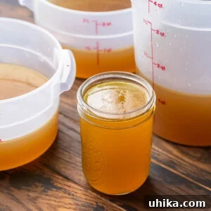 Liquid Gold Beef Stock 11 Featured image showing a mason jar filled with rich beef stock along with three large containers in the background, ready for storage.