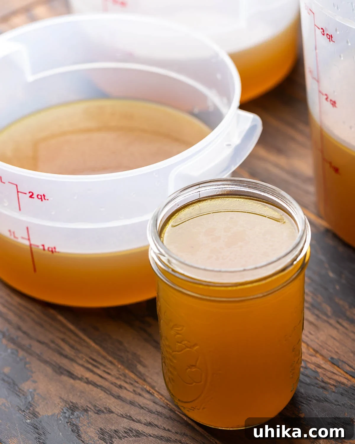 Liquid Gold Beef Stock 10 One mason jar filled with rich, clear beef stock along with three larger storage containers, partly filled and showing the golden hue of the liquid.