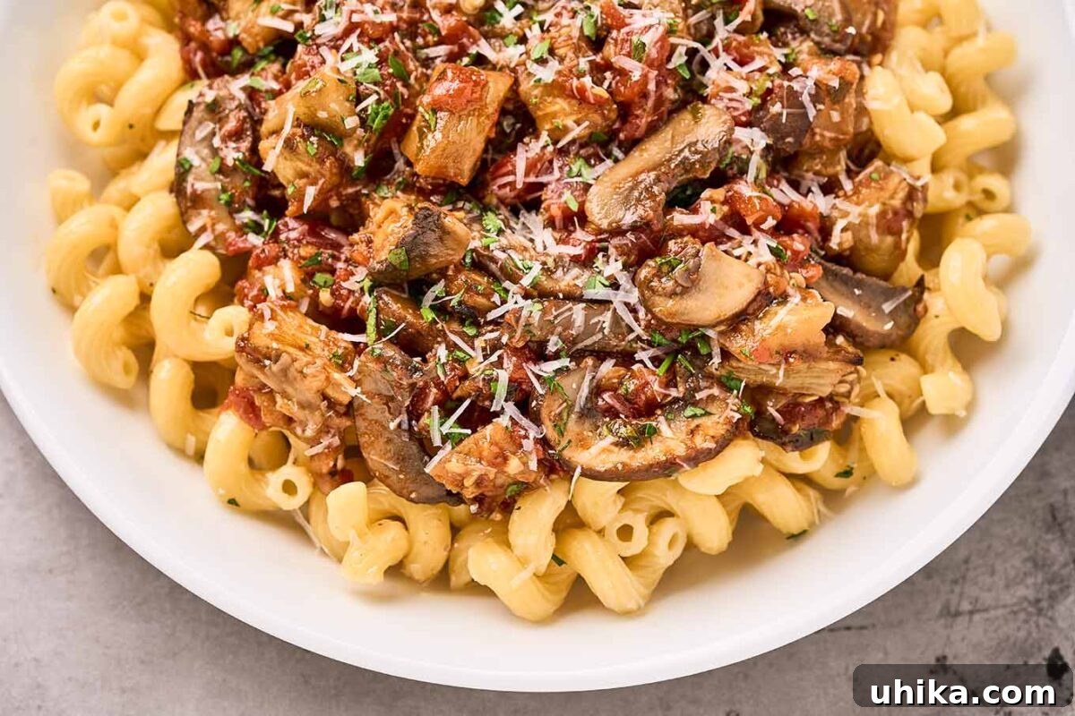 Savory Eggplant Mushroom Pasta 6 Close overhead view of a bowl of cavatappi pasta generously topped with a rich roasted eggplant, mushroom, and tomato sauce, garnished with grated Parmesan cheese and chopped fresh parsley.