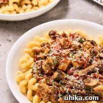 Two bowls of eggplant and mushroom tomato ragu over cavatappi pasta, a sprinkling of finely grated Parmesan cheese and chopped parsley on top, metal grater in the background.