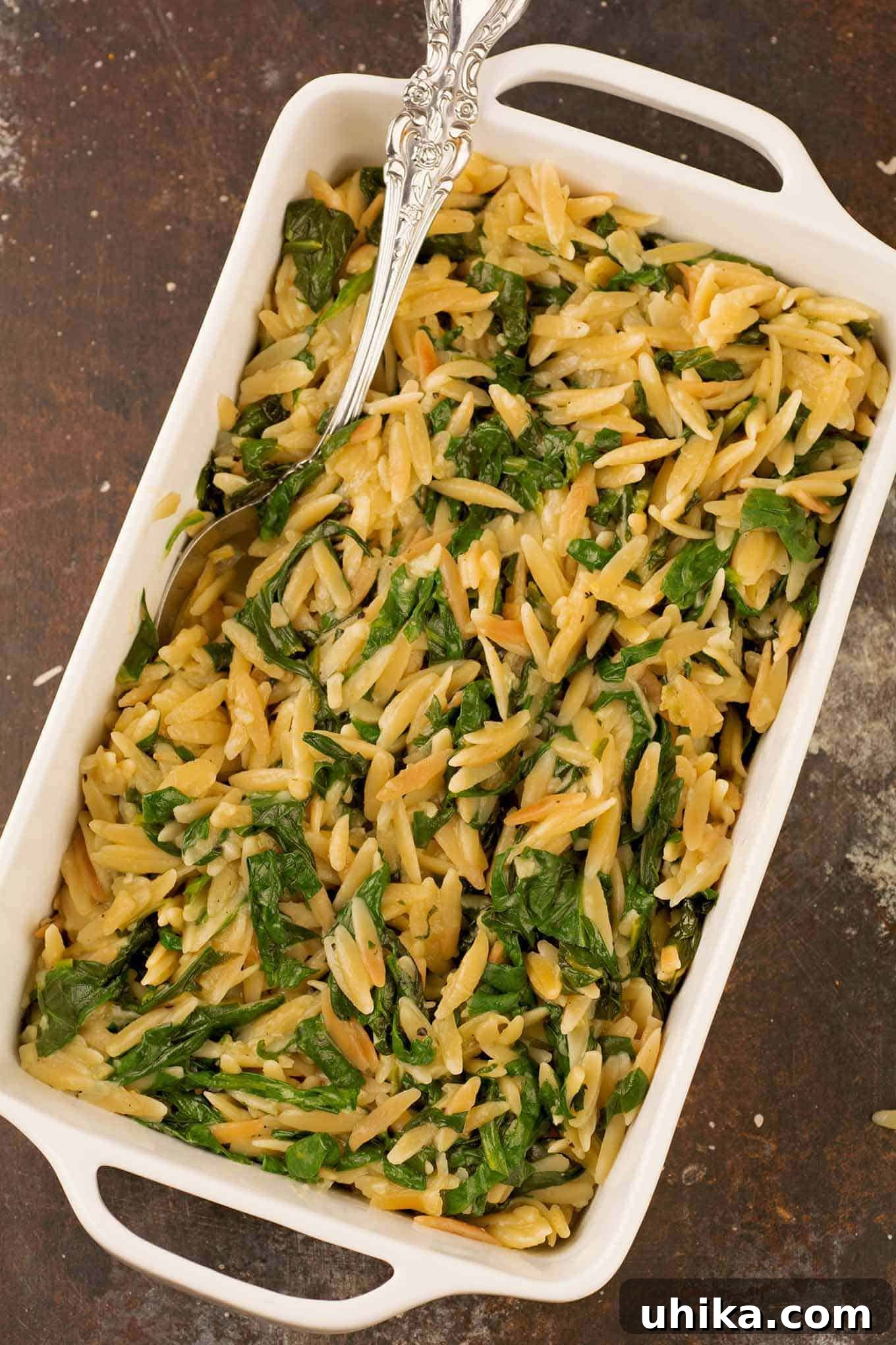Aromatic Toasted Garlic Orzo with Spinach 2 An overhead view of a casserole of toasted orzo and sautéed spinach side dish, with a serving spoon.