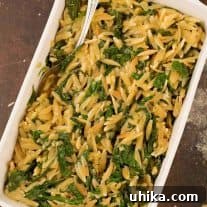 An overhead view of a casserole of toasted orzo and sautéed spinach side dish, with a serving spoon.
