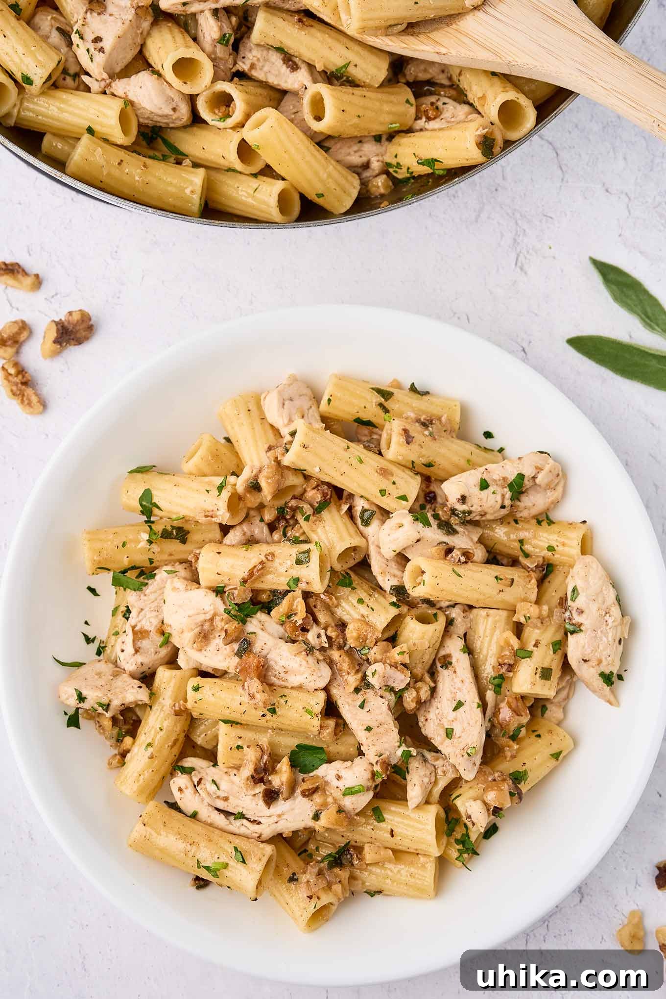 Nutty Brown Butter Chicken Pasta 2 An overhead view of brown butter chicken pasta being spooned into a serving bowl from the skillet. Golden pasta, tender chicken strips, and flecks of sage and walnuts are visible.
