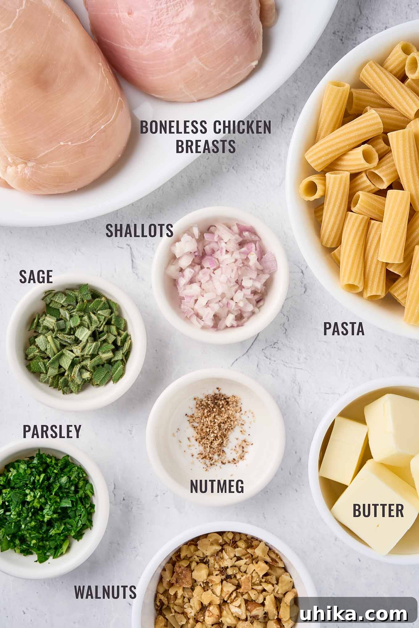 Nutty Brown Butter Chicken Pasta 3 A labeled, overhead view of the ingredients for brown butter pasta with chicken; boneless chicken breasts, rigatoni, shallots, sage, parsley, nutmeg, butter, and walnuts.