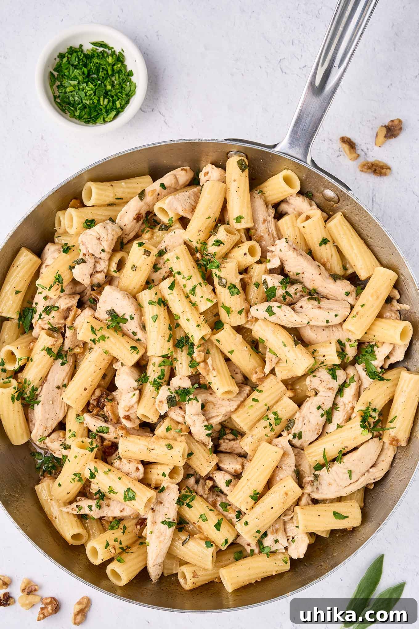 Nutty Brown Butter Chicken Pasta 9 An overhead view of a skillet filled with brown butter pasta and tender strips of chicken, garnished with parsley - a prep bowl with more chopped parsley to the side.