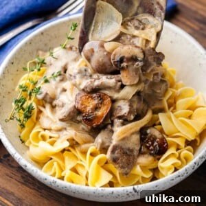 Velvety Beef Stroganoff 8 Beef stroganoff featured image with wooden spoon pouring gravy over egg noodles in white bowl.