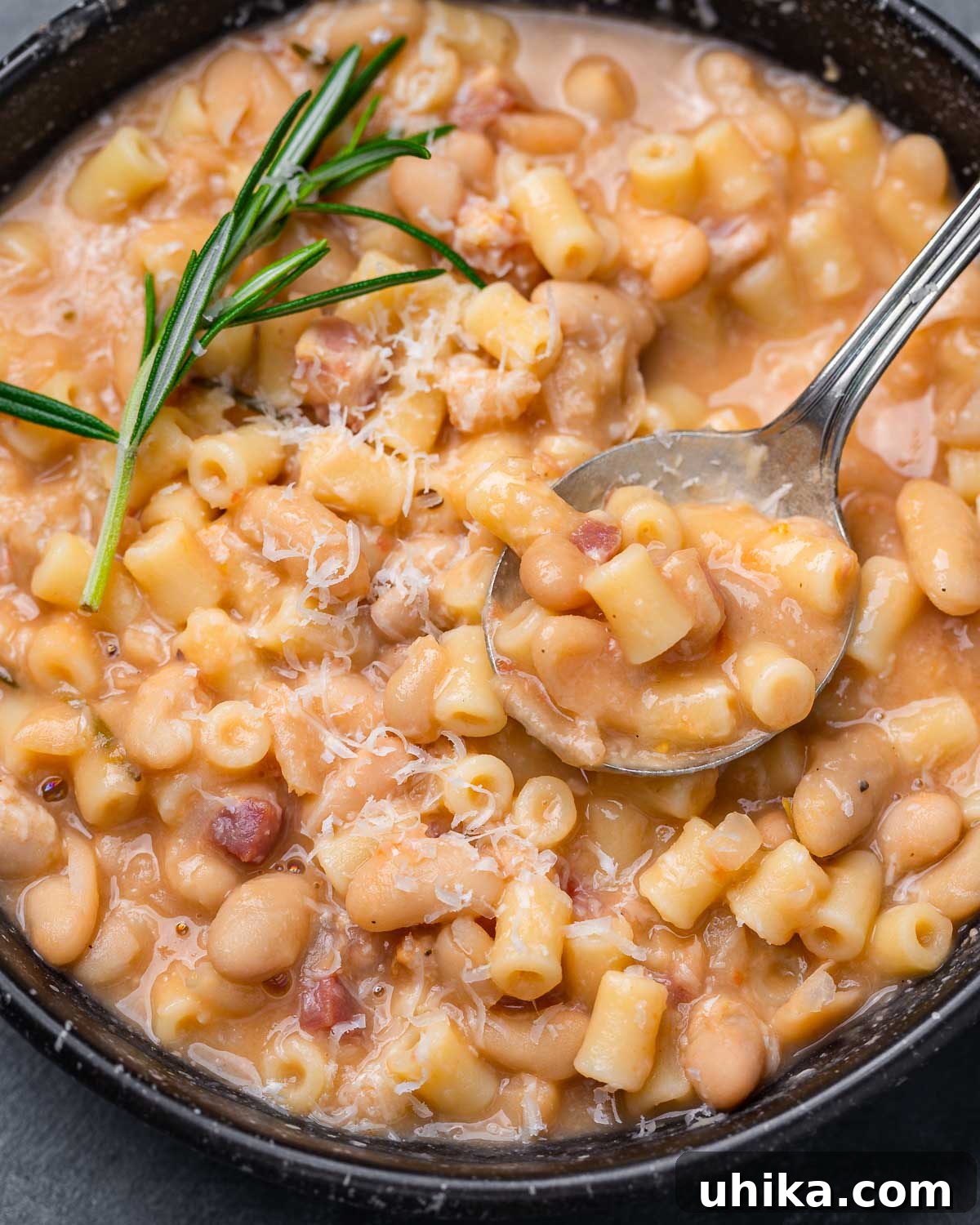 Pasta e Fagioli: Italy's Soul-Warming Classic 2 A rustic black bowl filled with steaming Pasta e Fagioli, garnished with a fresh sprig of rosemary and a spoon resting inside.