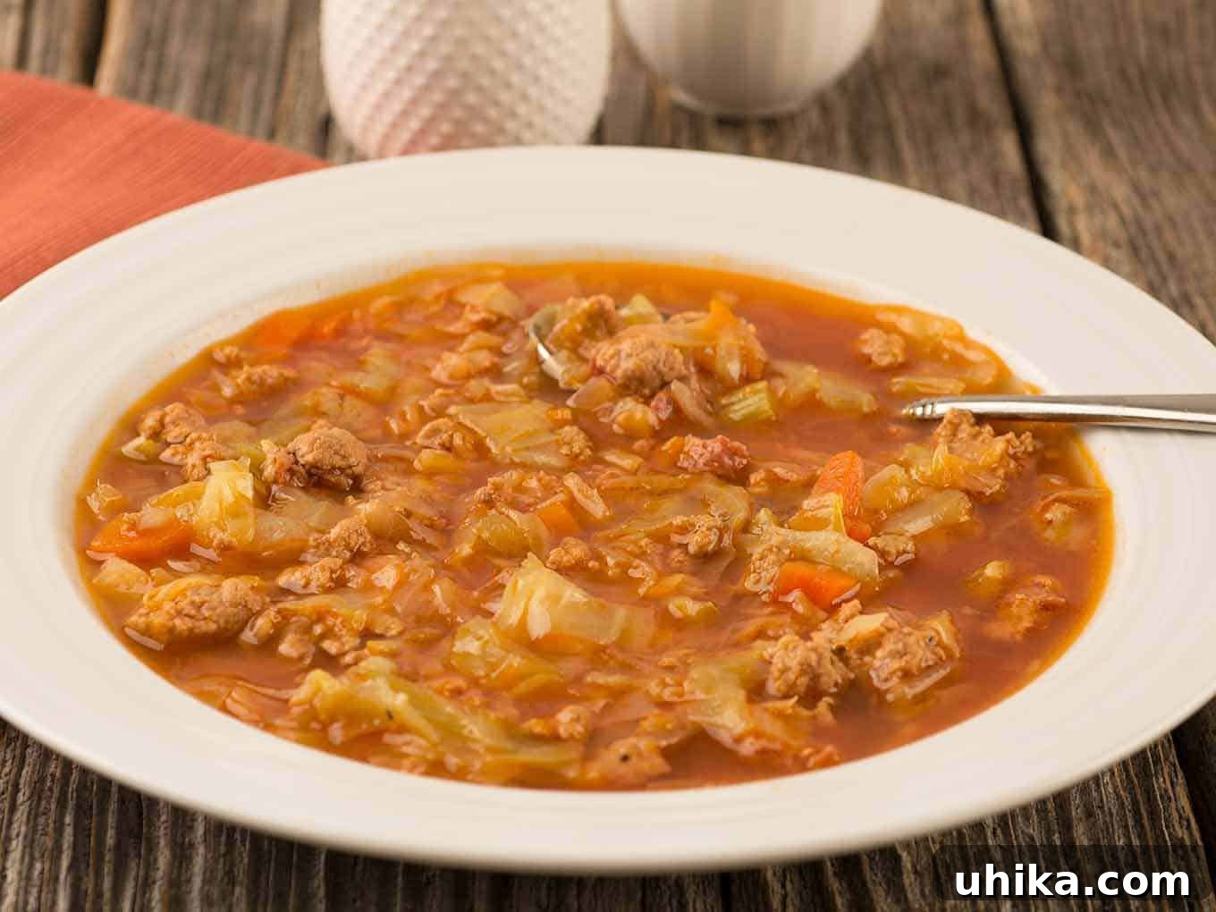 Quick Cabbage Comfort 3 A bowl of soup with crumbled ground turkey, smoked sausage, and cabbage in a tomato-based broth, napkin and white salt and pepper shakers in the background.