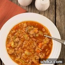 Quick Cabbage Comfort 5 An overhead view of Instant Pot cabbage, ground turkey and smoked sausage soup in a bowl with a spoon on a rustic wooden surface.