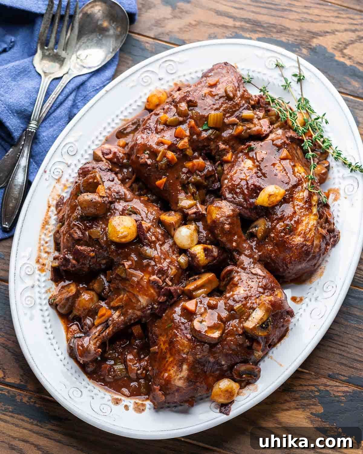 Classic French Wine-Braised Chicken 7 Overhead shot of Coq au Vin in a white serving platter garnished with fresh thyme, placed on a rustic wood table, with a side of crusty bread.