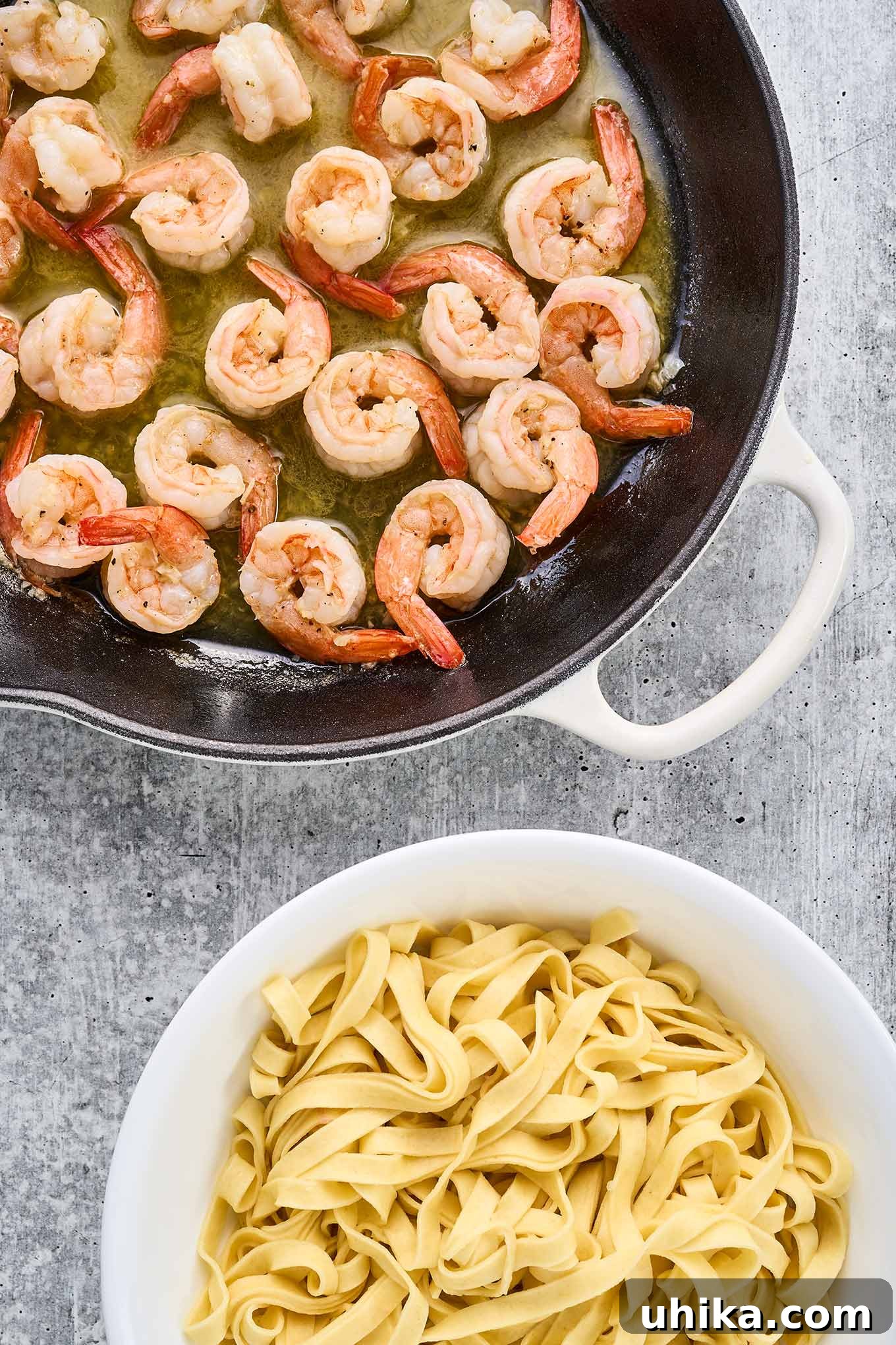 Vibrant Lime Garlic Shrimp Pasta 4 A cast iron pan with sautéed shrimp in butter sauce next to a bowl of fresh fettuccine, ready to be combined for garlic lime shrimp pasta.