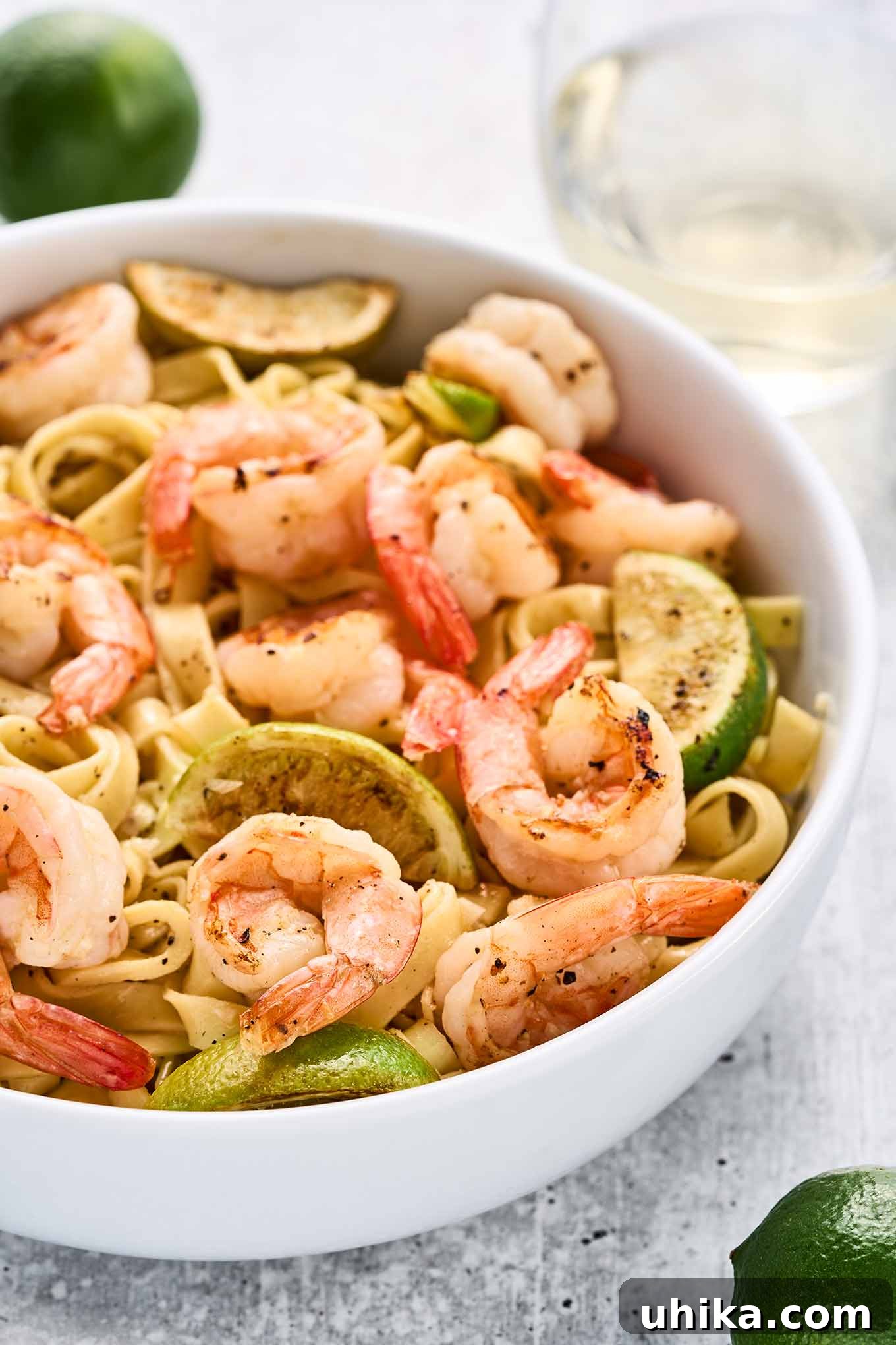 Vibrant Lime Garlic Shrimp Pasta 5 Close view of garlic lime shrimp tossed with fettuccine, showcasing the plump shrimp, pan-seared lime wedges, and tender pasta in a white bowl, ready for serving.