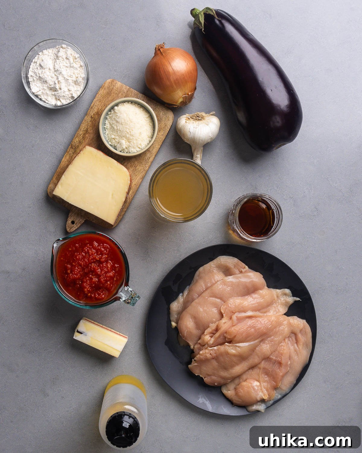 Classic Chicken Sorrentino 3 All ingredients for Chicken Sorrentino displayed: all-purpose flour, fontina cheese, Parmigiano Reggiano, onion, eggplant, garlic, chicken stock, dry Marsala wine, plum tomatoes, unsalted butter, chicken breasts, and extra virgin olive oil.
