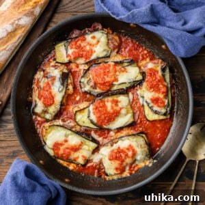 Chicken Sorrentino in a black pan with blue napkins and a loaf of Italian bread on the side.