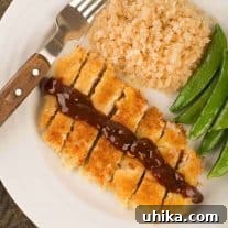 An overhead view a plate with Japanese breaded pork cutlet, sliced and topped with a drizzle of katsu sauce, served with riced cauliflower and sautéed snap peas.